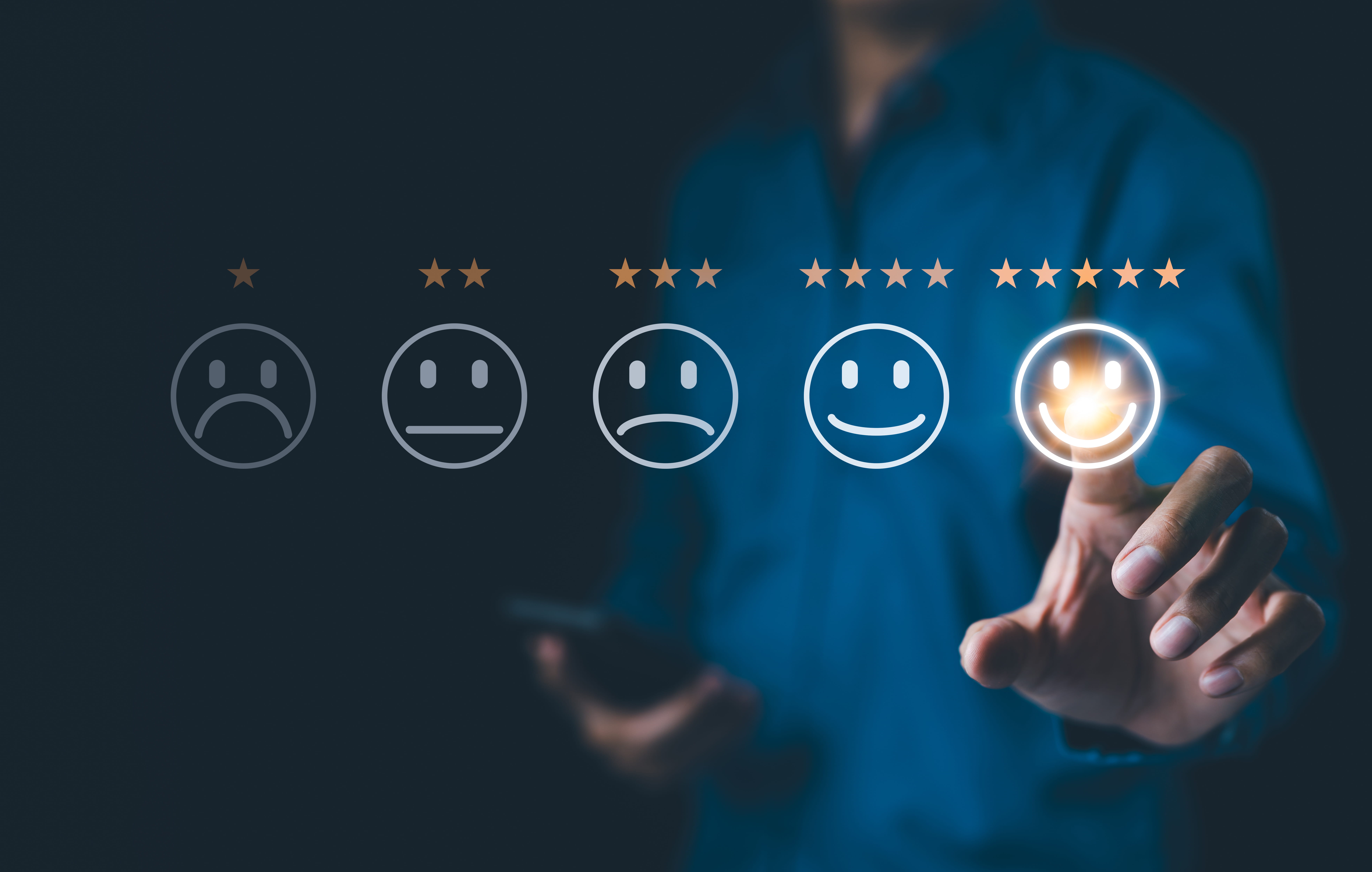 Line of different smiley faces indicating a rating of 1-5, with a person standing behind them choosing the five star rating.